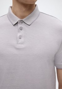 Ανοιχτό γκρι πόλο μπλουζάκι κατασκευασμένο από υφασμάτινο ύφασμα με υφή, με κλασικό γιακά, τέσσερα κουμπιά και διακριτικές ραφές στον γιακά.