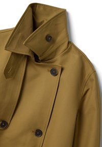 Trench-coat beige à double boutonnage avec col large à revers et boutons marron foncé, présenté à plat sur un fond blanc.