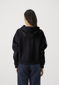 Zwarte hoodie met een relaxed fit, voorzien van ribgebreide manchetten en zoom, gemaakt van zachte stof. Logo-detail op de mouw.