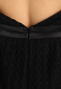 Vue arrière d'une robe en dentelle noire avec une fermeture éclair verticale et une ceinture en satin révélant la peau du haut du dos.