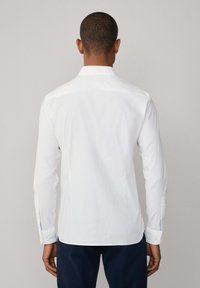 White long-sleeve shirt with a pointed collar, button cuffs, and a smooth texture. Features a straight hem and subtle stitching details.