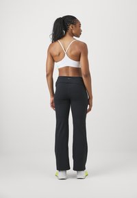 White sports bra with adjustable straps, paired with black flared workout pants. The outfit features a branded waistband and a smooth texture.