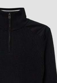 Schwarzer Pullover mit hohem Kragen, Reißverschluss, strukturiertem Strickkörper und glatten schwarzen Stoffakzenten an den Schultern.