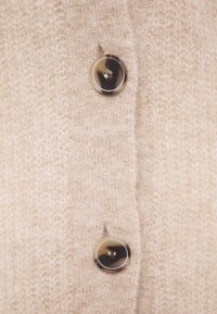 Beżowy dziany kardigan o miękkiej teksturze, z dwoma dużymi, okrągłymi guzikami z subtelnym marmurkowym wzorem, umieszczonymi na środku przodu.