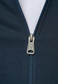 Marinekleurige dichtgemaakte kleding met een metalen ritsgrepen met gegraveerd ontwerp, die de geribbelde stofstructuur eronder toont.