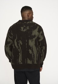 Dunkelbrauner und grüner gestrickter Pullover mit einem pixelierten Muster, runder Ausschnitt und leicht oversized Passform. Strukturierte Oberfläche.