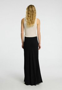 Zwarte maxi-rok van een soepele, vloeiende stof, gecombineerd met een strakke beige tanktop. Het ontwerp is eenvoudig en minimalistisch, met duidelijke lijnen.