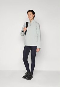 Ανοιχτό γκρι ζακέτα με φερμουάρ, εφαρμοστά μαύρα κολάν και μαύρα ορειβατικά μποτάκια. Η ζακέτα έχει κουκούλα και κομψό σχέδιο, κατάλληλο για υπαίθριες δραστηριότητες.