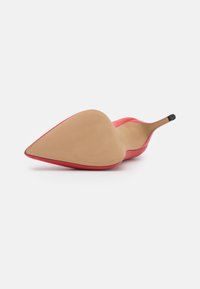 Chaussure à talon haut rouge avec un bout pointu et une tige en cuir lisse. Semelle extérieure beige dotée d'un motif antidérapant texturé et d'un talon fin avec une pointe noire.