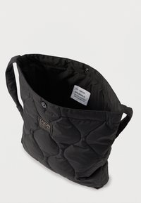 Saco tote preto acolchoado com textura almofadada, alças duplas e etiqueta interior. Possui um fecho de pressão para armazenamento seguro.