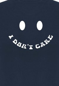 T-shirt marine avec un grand motif de smiley blanc comportant deux yeux creux et le texte "JE M'EN FOUS" dans une police originale en dessous.