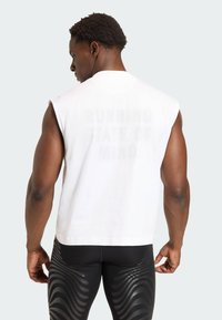 Valkoinen hihaton t-paita, jossa on rohkea, haalistunut painatus selässä, jossa lukee "RUNNING STATE OF MIND", yhdistettynä mustiin kuvioituihin legginsseihin.