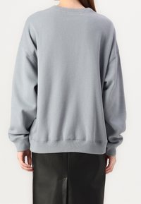 Ljust grå oversized sweatshirt med ribbade ärmslut och nederkant, som har en rund hals och mjukt, strukturerat tyg, matchad med en svart kjol.