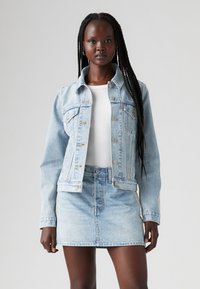 Giacca di jeans azzurro chiaro con colletto e tasche frontali, abbinata a una gonna di jeans coordinata. Presenta un design aderente e lievi strappi.