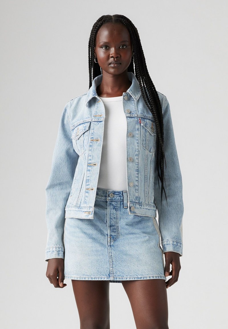 Giacca di jeans azzurro chiaro con colletto e tasche frontali, abbinata a una gonna di jeans coordinata. Presenta un design aderente e lievi strappi.