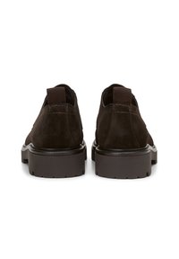 Chaussures en daim marron avec une semelle en caoutchouc robuste, présentant une texture lisse et des accents cousus. La vue arrière montre une coupe basse et un détail de tirant.