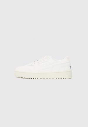 Baskets blanches avec une tige en cuir lisse, un bout perforé et des accents texturés. Elles disposent d'une épaisse semelle en caoutchouc et d'un détail de marque minimal.