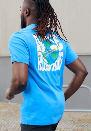 Homme aux dreadlocks faisant du jogging, portant un t-shirt bleu avec un globe et le texte « Just Running » dans le dos.