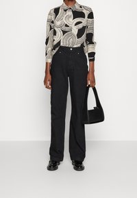 Mustat vyötäröltä korkealla olevat farkut yhdistettynä kuvioituun puseroon, jossa on kerma- ja musta väri, kaulus ja pitkät hihat. Pidä mustaa käsilaukkua.