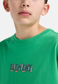 Groene katoenen T-shirt met een grafische print in blokletters in groen, wit en oranje. Korte mouwen en ronde hals.