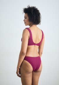 Biquíni roxo texturizado com costas em formato de scoop e alças largas. Parte de baixo de cintura alta destaca um acabamento suave. Design simples e funcional.