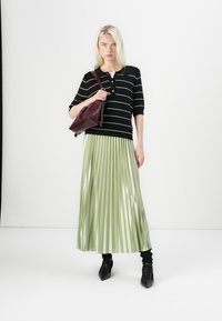 Top à rayures noir et blanc, jupe plissée vert clair, sac bordeaux et chaussures pointues noires. Textures lisses et design superposé.