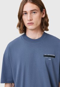 Grå bomulds t-shirt med korte ærmer, rund hals og en forlommet med grafisk tekst i sort og hvid.