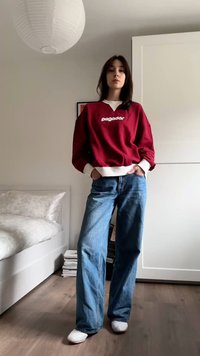 Μαρούνο φούτερ με λευκό λογότυπο, σε συνδυασμό με μπλε τζιν παντελόνι με φαρδιά πόδια. Το μοντέλο στέκεται σε δωμάτιο με ξύλινα πατώματα και ελαφριά κουβέρτα.