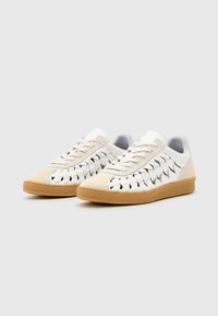 Scarpe sportive bianche con tomaia in suede e pelle, caratterizzate da dettagli intrecciati sui lati e una suola in gomma testurizzata. Design con lacci.