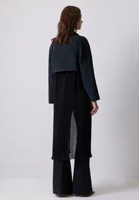 Black two-piece outfit featuring a cropped top with a smooth texture and flared pants with a pleated design, tailored for a loose fit.
