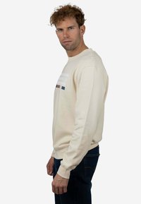 Sudadera beige con cuello redondo, puños acanalados y un gráfico frontal que presenta franjas horizontales en varios colores.