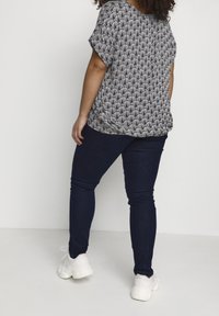 Haut à motifs noir et blanc avec des manches courtes, assorti à un jean skinny bleu foncé. Des baskets blanches complètent la tenue.