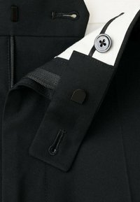 Veste en tissu noir avec un col blanc, dotée d'une fermeture éclair, d'une fermeture à bouton et de détails de couture contrastés. Texture lisse avec un design minimaliste.