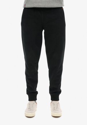 Sorte sweatpants med en tætsiddende pasform, lavet af blødt stof. Har elastisk talje og mansjetter. Båret med lysegrå sneakers.