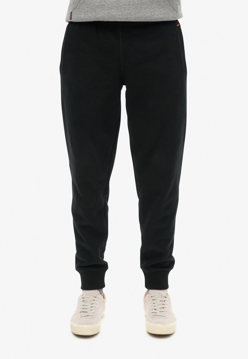 Zwarte joggingbroek gemaakt van zachte stof, met een losse pasvorm, elastische tailleband en geribbelde manchetten. Minimale branding op het been.