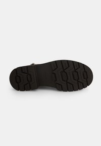 Suola in gomma nera con motivi di texture, caratterizzata da scanalature profonde e un profilo piatto per trazione e stabilità.