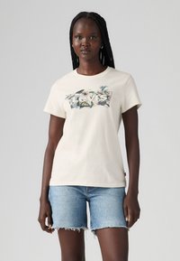 Tricou din bumbac crem, cu un grafic colorat al logo-ului Levi's, cu flori. Mâneci scurte, gât rotund și croială lejeră. Purtați cu pantaloni scurți din blugi albaștri.