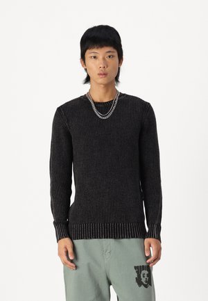 Suéter negro de canalé con mangas largas, tejido texturizado, escote redondo y un dobladillo en contraste, combinado con pantalones de corte relajado en verde claro.