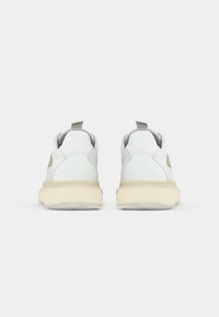Weiße Sneaker mit einem Obermaterial aus glattem Leder, beiger Sohle, runder Form und einem Zugtab am Fersenbereich. Keine sichtbaren Muster oder Akzente.