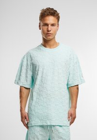 Mintgrønn teksturert oversized t-skjorte med korte ermer, med et mønstret overflate og rund hals. Ingen synlige merkevaredetaljer.