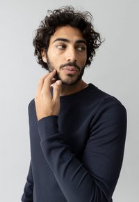 Sudadera de manga larga azul marino, hecha de un tejido suave. Presenta un cuello redondo y un emblema en la manga izquierda. Textura lisa.