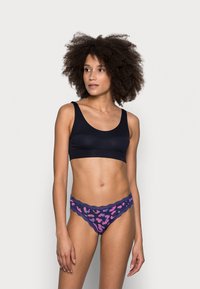Svart bralette i slätt material, tillsammans med lila leopardmönstrade trosor med spetskant och rosa detaljer, med en låg midja.