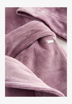 Material moale, texturat în roz pal. Include un eticheta metalică cu cuvântul „DOWNTIME.” Are o textură netedă și un design stratificat.