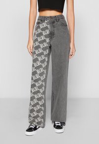 Grå vide ben jeans med ett sidan som har ett upprepande vitt mönster. Texturerat tyg, standard midjeband och design med fem fickor.