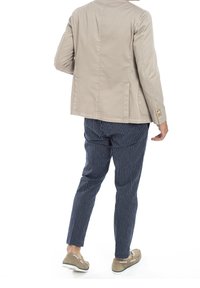 Ljusbeige bomullsjacka med enkel design, tillsammans med marinblå randiga byxor. Färdiga med avslappnade skor.