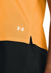 Top atlético naranja con un acabado texturizado, que presenta una abertura lateral y un logo de Under Armour en blanco. Usado sobre pantalones cortos negros.