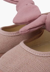Zapatos de tela rosas con una superficie texturada y tejida, que presentan un gran lazo en la parte frontal y un diseño de punta redonda.
