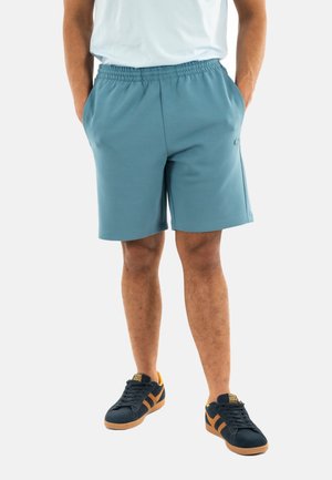 Pantalones cortos deportivos de color azul claro con cintura elástica, bolsillos laterales y una textura suave, combinados con zapatillas negras y naranjas.