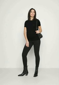 Svart kortermet skjorte, svarte leggings og svarte ankelstøvler. Modellen bærer en liten svart skulderveske og står mot en nøytral bakgrunn.