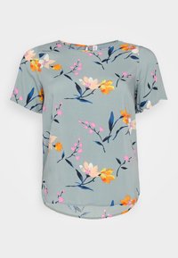 Blommig blus i mjukt tyg med en ljusblå bakgrund. Har livliga rosa, orange och gula blommor. Korta ärmar, rund halsringning.